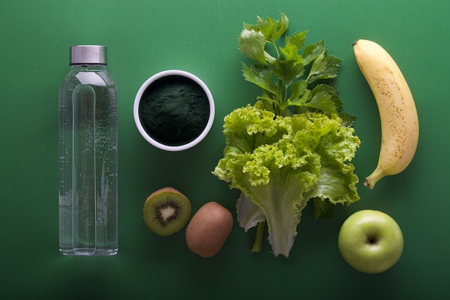 Image depicts vegetables, bottled water, fruits, and more for plant-based healthy diet.