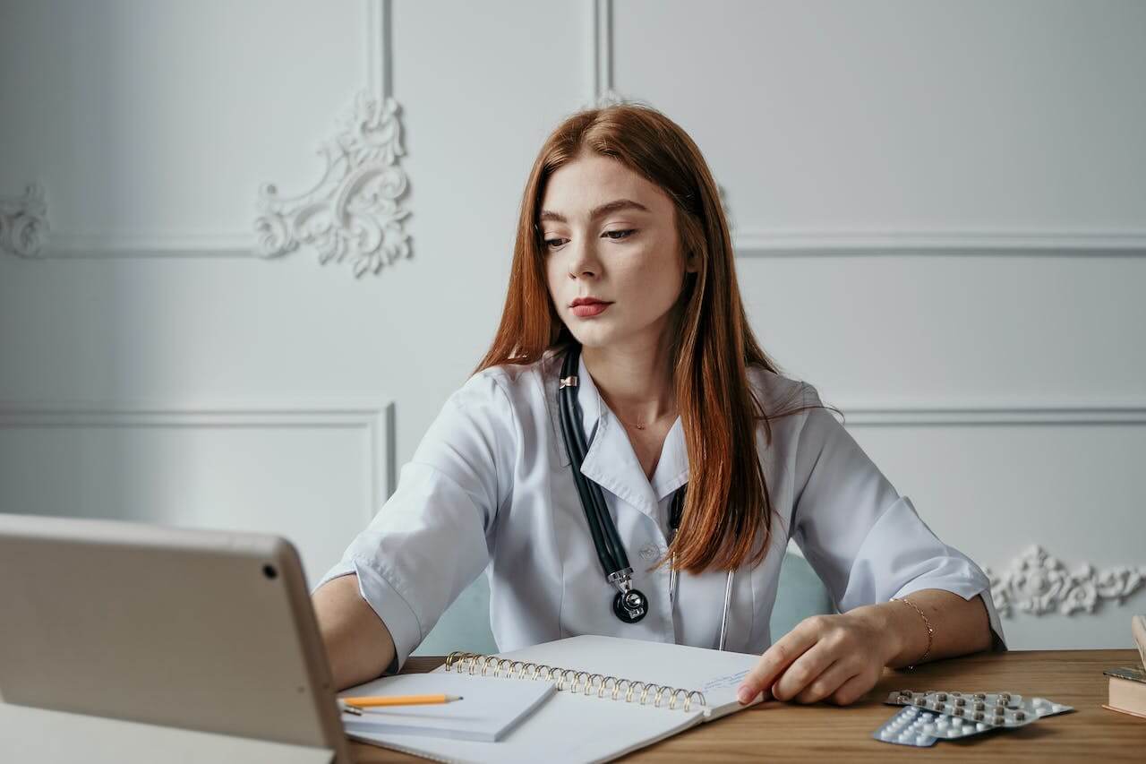 A lady medical practitioner typing on a laptop with notes.  